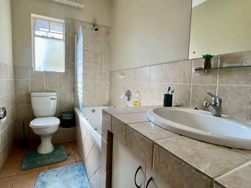 A functional bathroom featuring a built-in vanity with a ceramic basin, a bathtub with shower mixer, and neutral wall tiling.