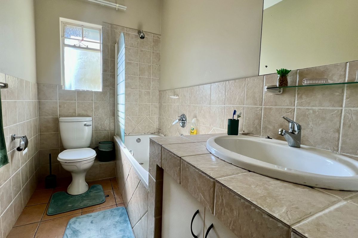 A functional bathroom featuring a built-in vanity with a ceramic basin, a bathtub with shower mixer, and neutral wall tiling.