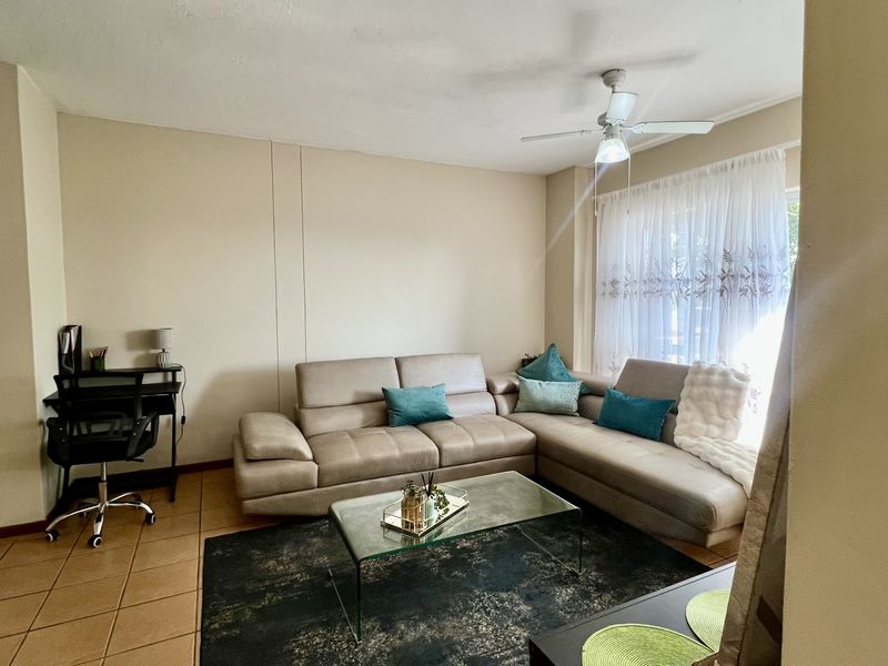 A comfortable living room featuring tiled flooring, a ceiling fan, and natural light through a sliding door.