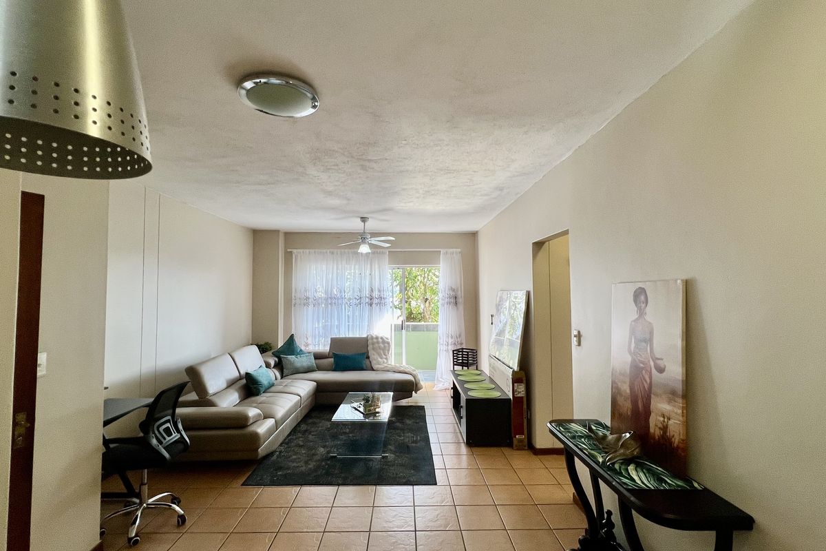 Spacious living room featuring tiled flooring, a ceiling fan, and a sliding glass door providing access to an outdoor balcony area.