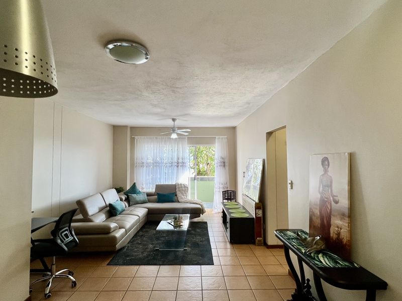 Spacious living room featuring tiled flooring, a ceiling fan, and a sliding glass door providing access to an outdoor balcony area.