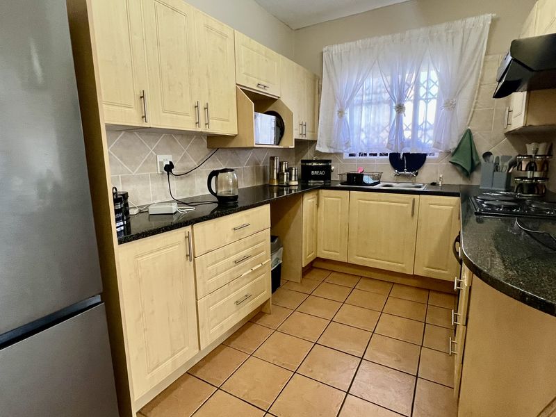 A functional kitchen featuring light wood-finish cabinetry, granite countertops, tiled backsplash, and ceramic floor tiles with a window overlooking the exterior.