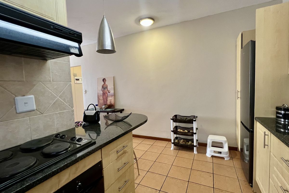 A functional kitchen featuring light wood cabinetry, granite countertops, a built-in electric hob with extractor fan, and tiled flooring.