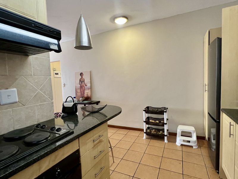 A functional kitchen featuring light wood cabinetry, granite countertops, a built-in electric hob with extractor fan, and tiled flooring.