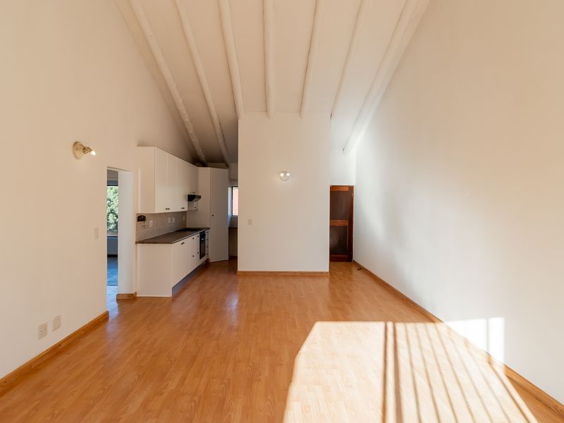 Spacious open-plan living area featuring high vaulted ceilings with exposed beams, laminate flooring, and a functional kitchen with built-in cabinetry and appliances.