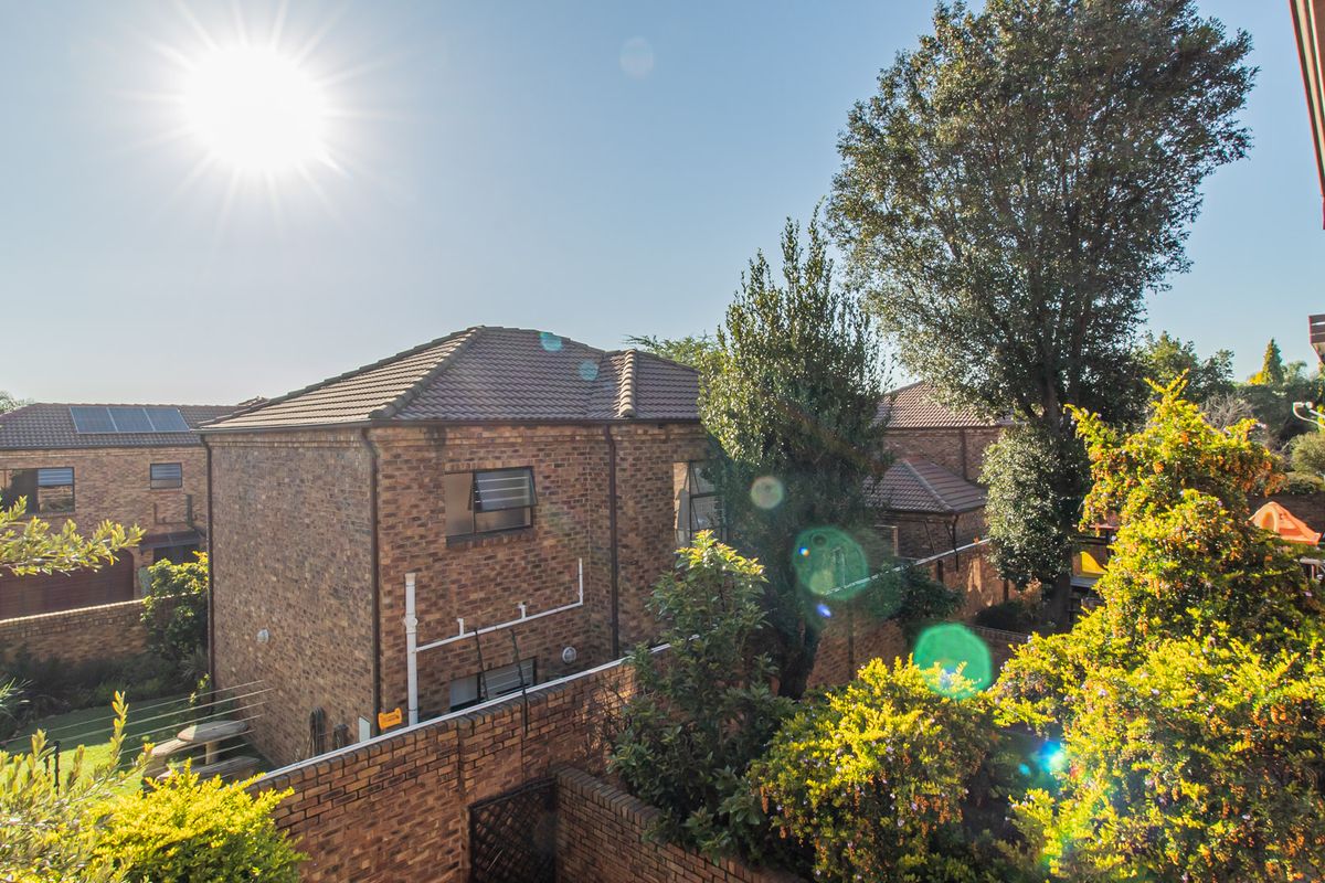An elevated view of the rear exterior of the townhouse complex, featuring face brick construction, tiled roofing, and established garden surroundings.