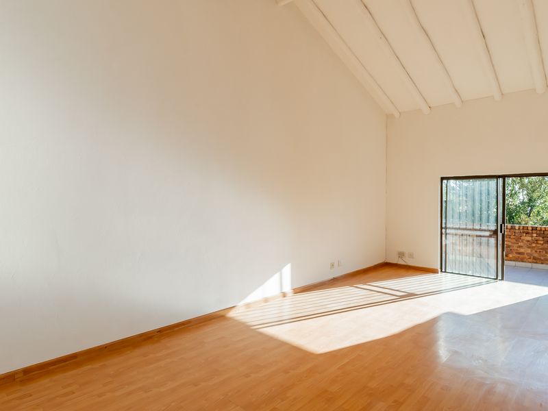 Spacious living area featuring vaulted ceilings with exposed beams, laminate flooring, and a sliding glass door leading to an outdoor balcony.