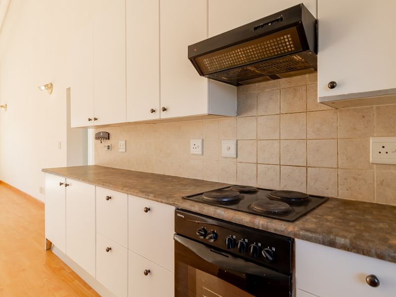 A clean, functional kitchen featuring white cabinetry, laminate countertops, and integrated cooking appliances, set within an open-plan living space.