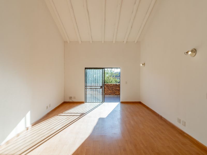 A bright, empty living room featuring high exposed beam ceilings, laminate flooring, and a sliding glass door leading to an outdoor area.