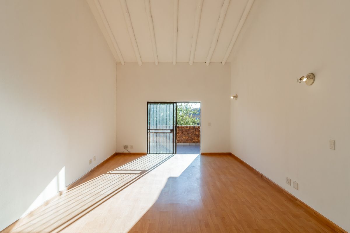 A bright, empty living room featuring high exposed beam ceilings, laminate flooring, and a sliding glass door leading to an outdoor area.