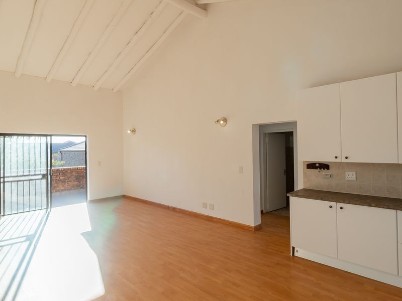 Spacious open-plan living area featuring vaulted ceilings with exposed beams, laminate flooring, and a functional kitchen with built-in cabinetry and direct patio access.