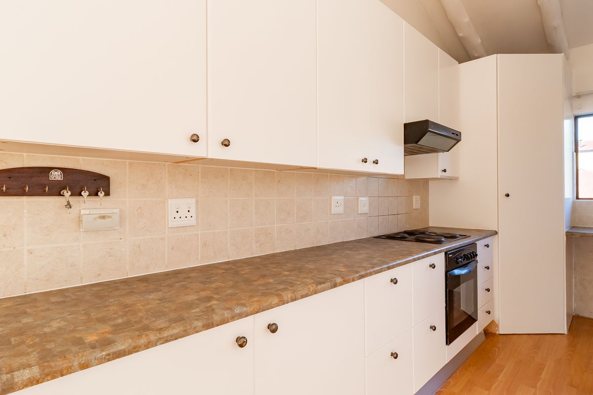 A clean, functional kitchen featuring white cabinetry, laminate countertops, tiled backsplash, and integrated cooking appliances with natural light from a side window.