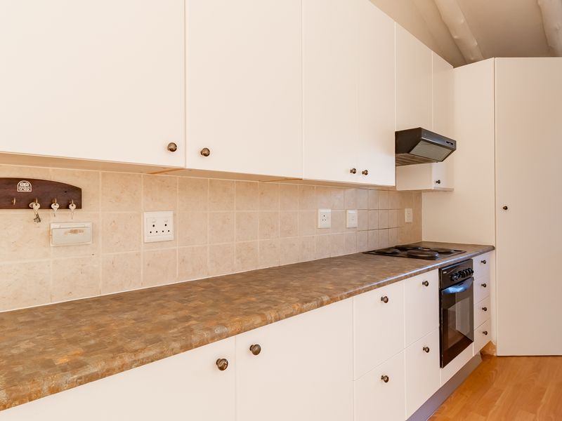 A clean, functional kitchen featuring white cabinetry, laminate countertops, tiled backsplash, and integrated cooking appliances with natural light from a side window.