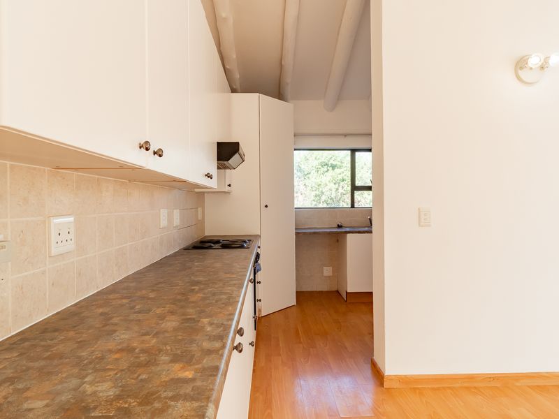 A functional kitchen featuring laminate countertops, built-in cabinetry, a tiled backsplash, and exposed ceiling beams, offering a clean and practical workspace.