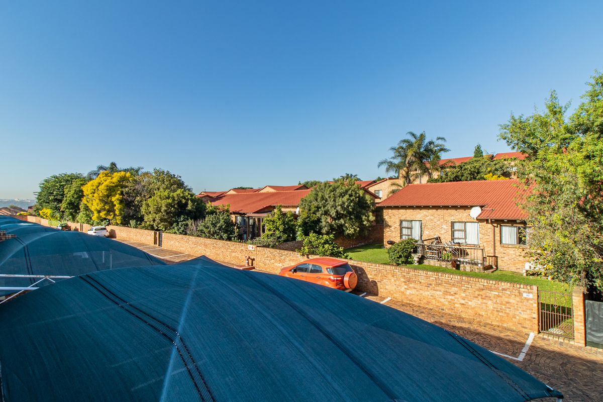 An elevated view of a townhouse complex featuring brick-faced units with tiled roofs, paved driveways, and shaded parking structures.