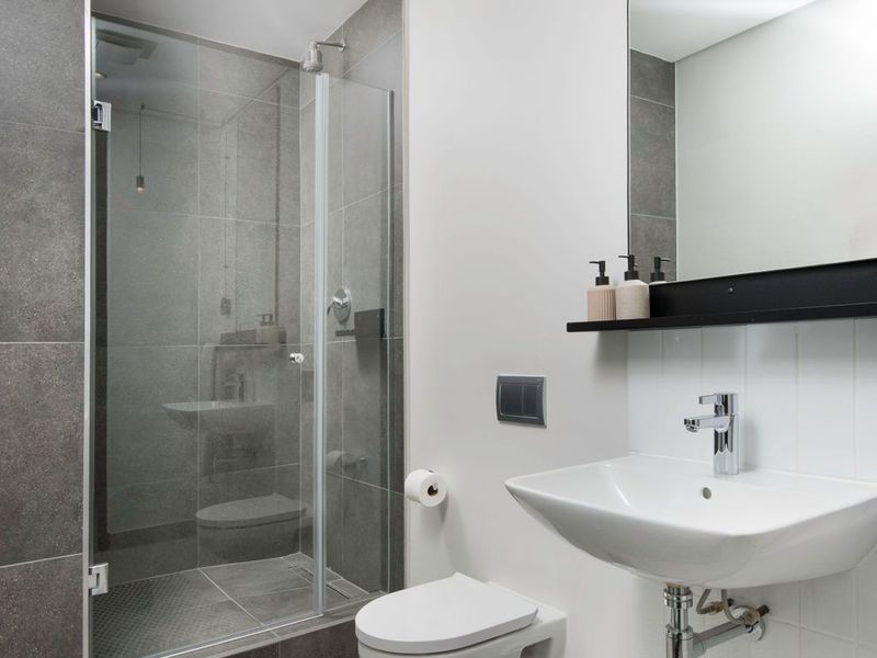 Modern bathroom featuring a wall-mounted basin, wall-hung toilet, and a spacious glass-enclosed shower with contemporary grey tiling.