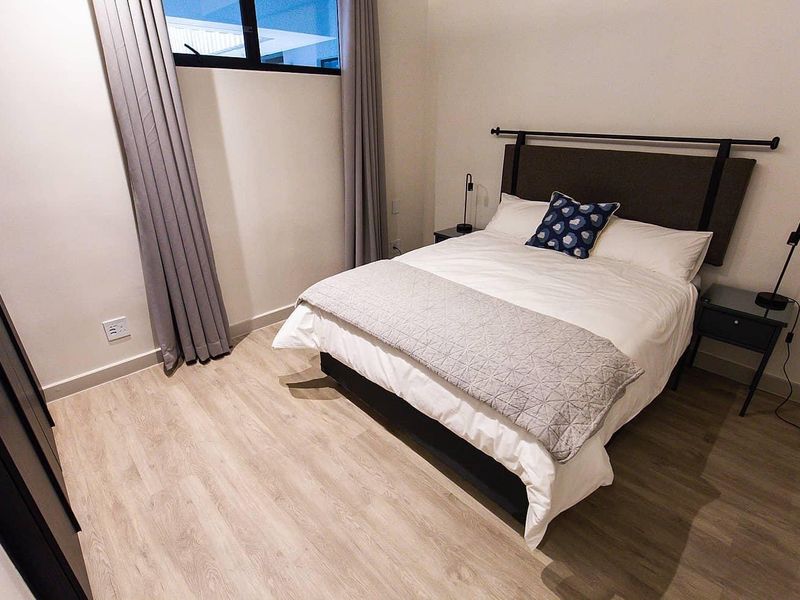 A well-maintained bedroom featuring light-toned laminate flooring, a built-in wardrobe, and a top-hung window with neutral curtains.