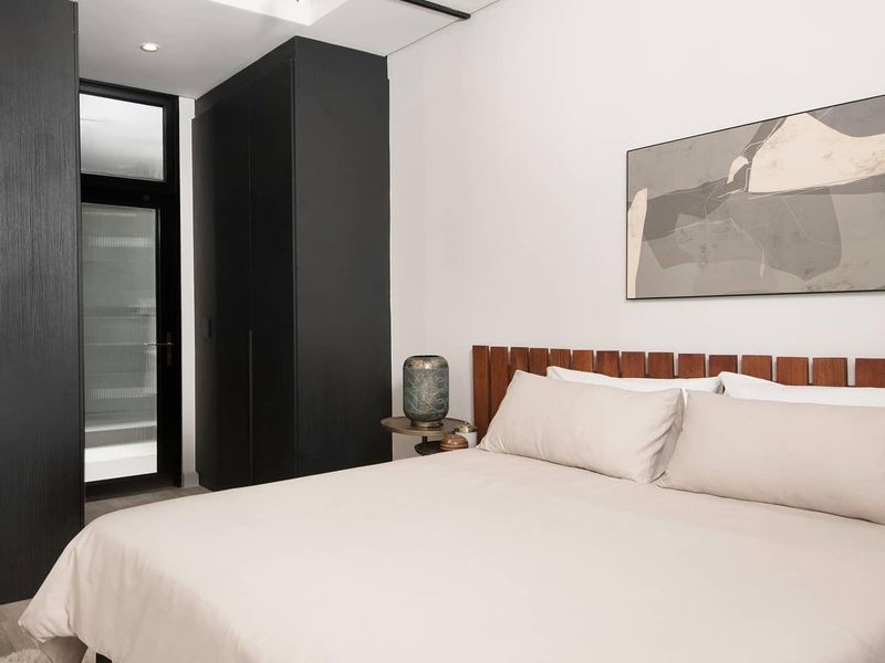 Modern bedroom featuring built-in black cabinetry, exposed concrete ceiling details, track lighting, and a glass panel door leading to an outdoor area.