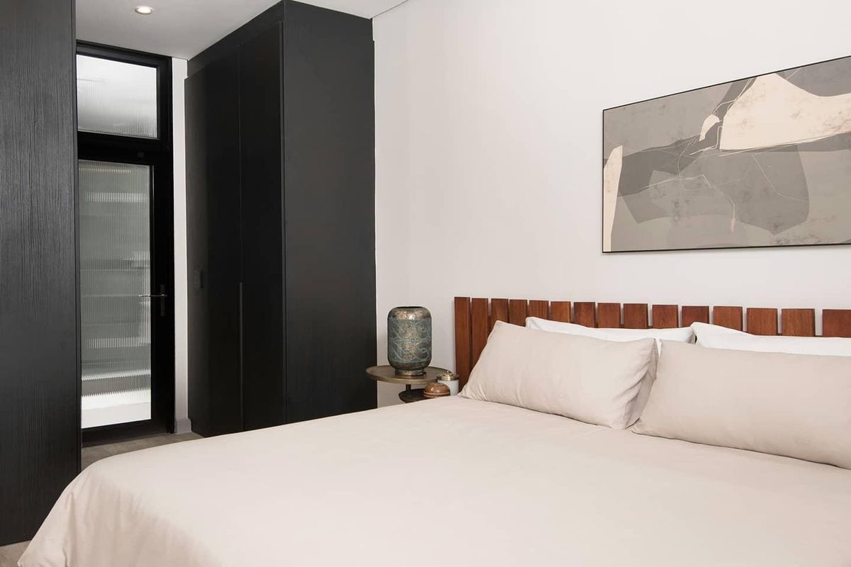 Modern bedroom featuring built-in black cabinetry, exposed concrete ceiling details, track lighting, and a glass panel door leading to an outdoor area.