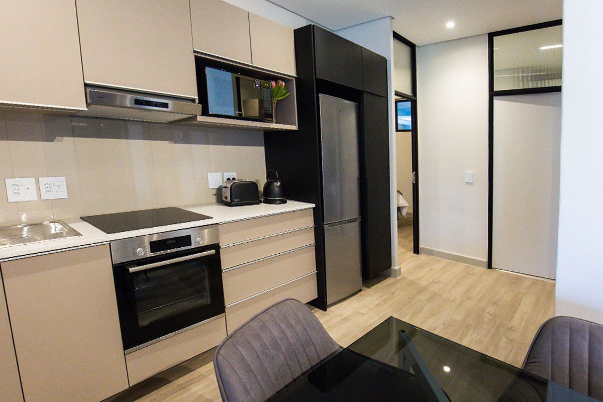 Modern kitchen featuring sleek cabinetry, integrated appliances including an oven and hob, and durable laminate flooring in an open-plan layout.
