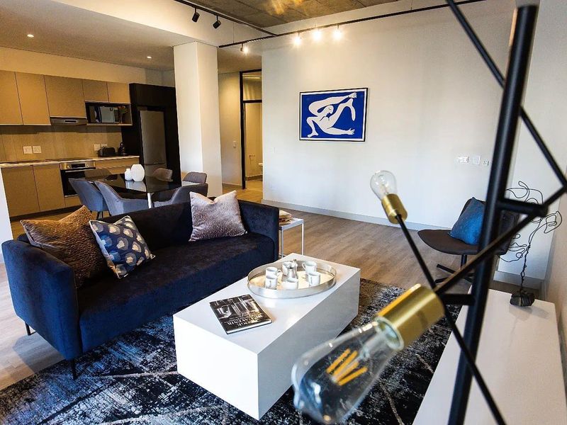 Modern open-plan living area featuring a sleek kitchen with integrated appliances, exposed concrete ceilings, and contemporary track lighting throughout the space.