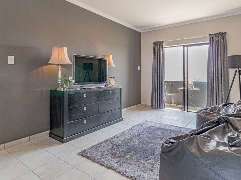 A well-maintained living room featuring neutral tiled flooring, a dark accent wall, and direct access to a private balcony through sliding glass doors.