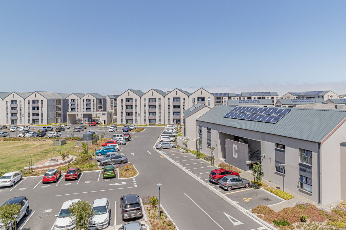 Aerial view of a modern apartment complex featuring multiple residential blocks, paved parking areas, and solar panel installations on the roofs.