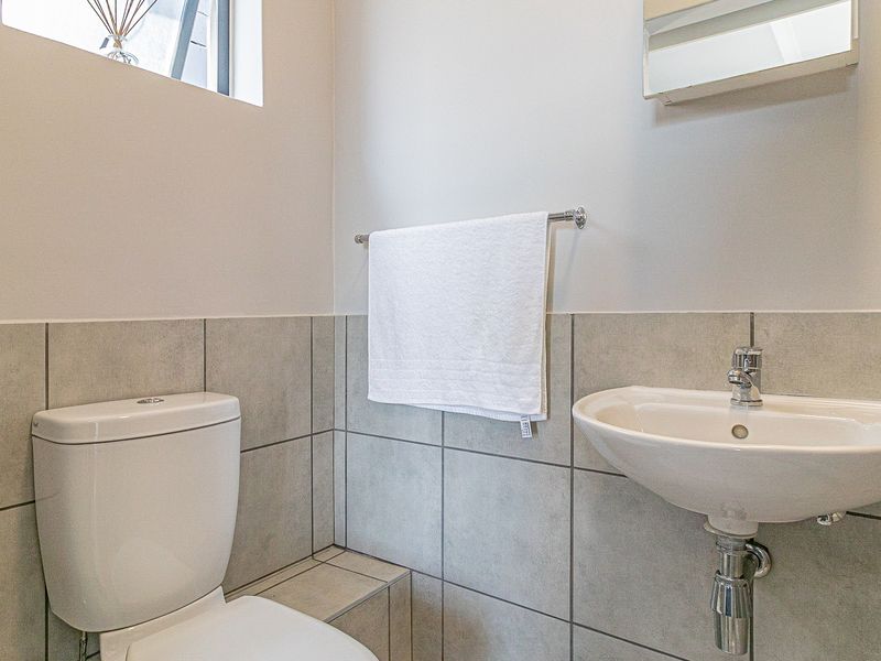 A clean and functional bathroom featuring a wall-mounted basin, modern toilet, and neutral tiled splashback.