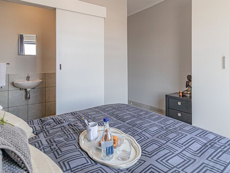 A well-maintained bedroom featuring a built-in wardrobe and an en-suite bathroom area with a wall-mounted basin and tiled finishes.