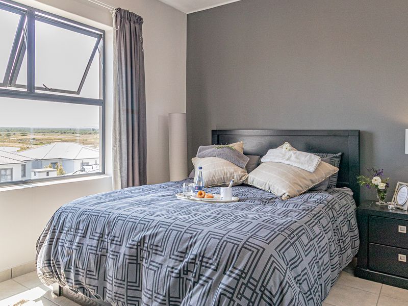 A well-lit bedroom featuring neutral tones, an accent wall, and a large top-hung window providing natural light and exterior views.