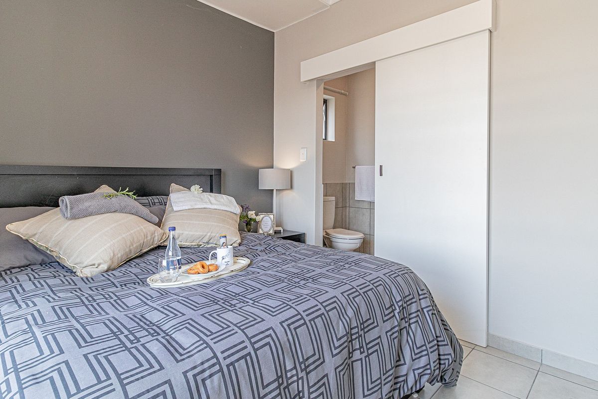 A well-maintained bedroom featuring a modern sliding door leading to an en-suite bathroom, neutral color palette, and tiled flooring.