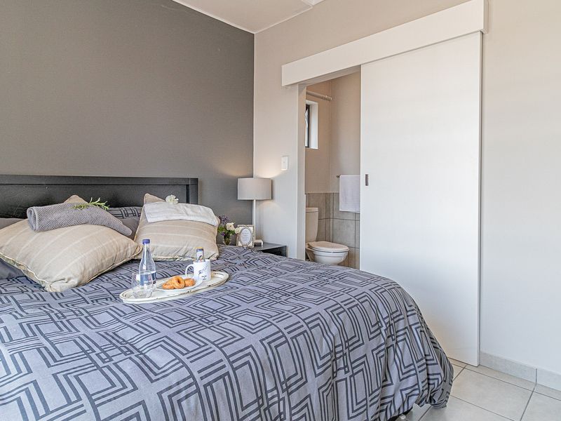 A well-maintained bedroom featuring a modern sliding door leading to an en-suite bathroom, neutral color palette, and tiled flooring.