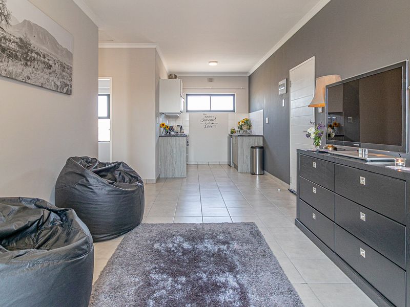 An open-plan living area featuring tiled flooring, a neutral color palette, and a functional kitchen space at the rear.