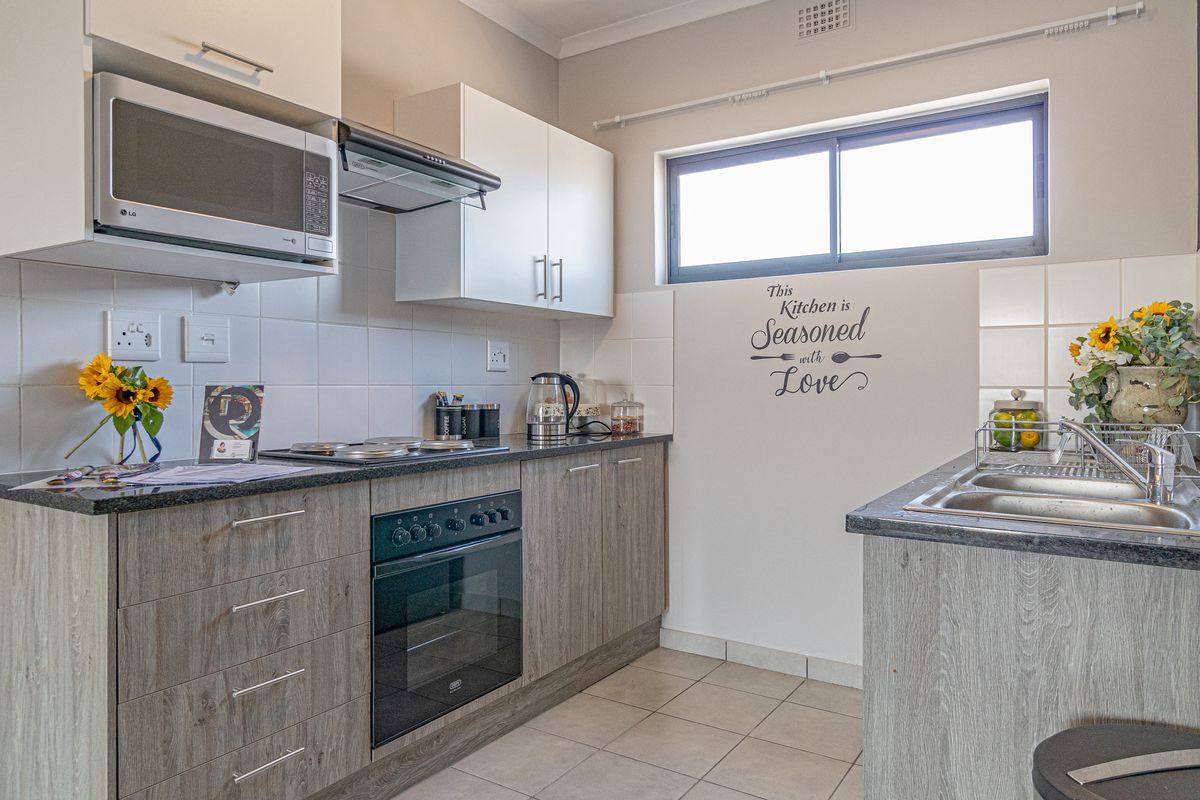 A well-maintained kitchen featuring modern laminate cabinetry, granite countertops, a built-in oven with hob, and a functional double sink setup.