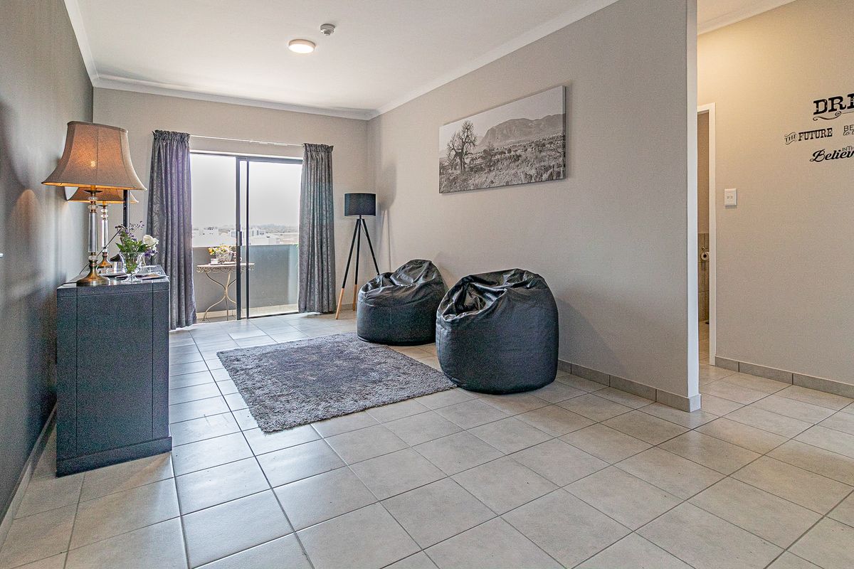 A bright living room featuring neutral tiled flooring, cove cornicing, and a sliding glass door providing access to an outdoor balcony area.