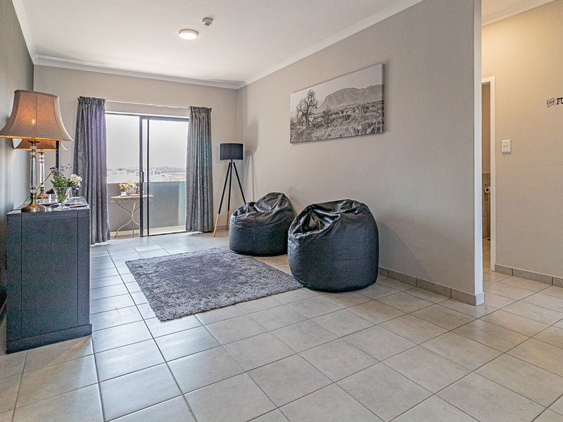 A bright living room featuring neutral tiled flooring, cove cornicing, and a sliding glass door providing access to an outdoor balcony area.