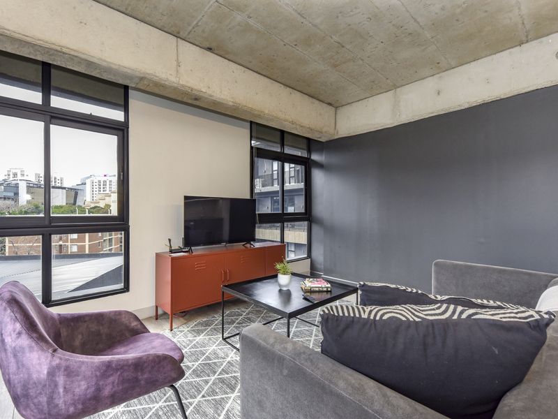 Modern living room featuring an industrial-style exposed concrete ceiling, large windows providing ample natural light, and contemporary finishes.