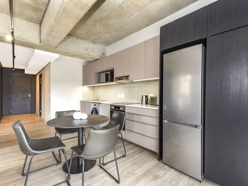 Modern open-plan kitchen featuring sleek cabinetry, integrated appliances, and an industrial-style exposed concrete ceiling, seamlessly flowing into the living area.