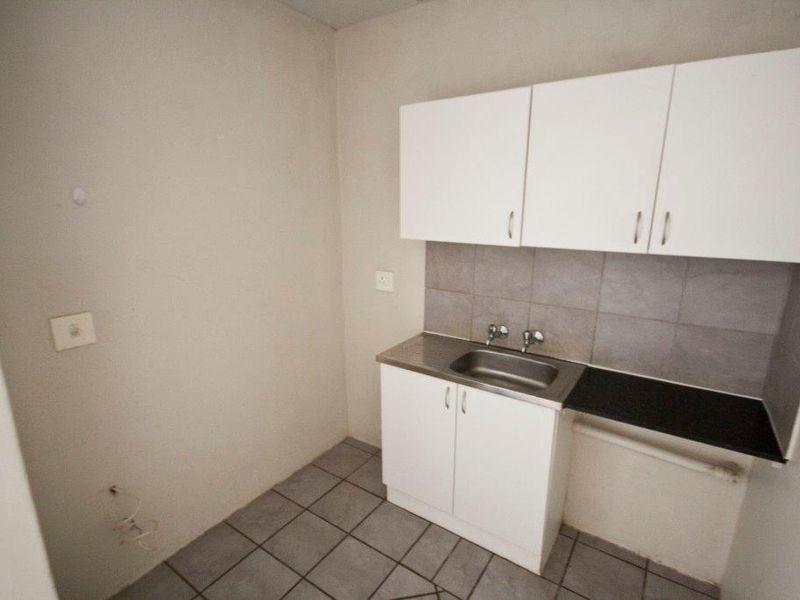 A compact kitchen area featuring white cabinetry, a stainless steel sink, tiled backsplash, and tiled flooring, providing a functional space for basic culinary needs.