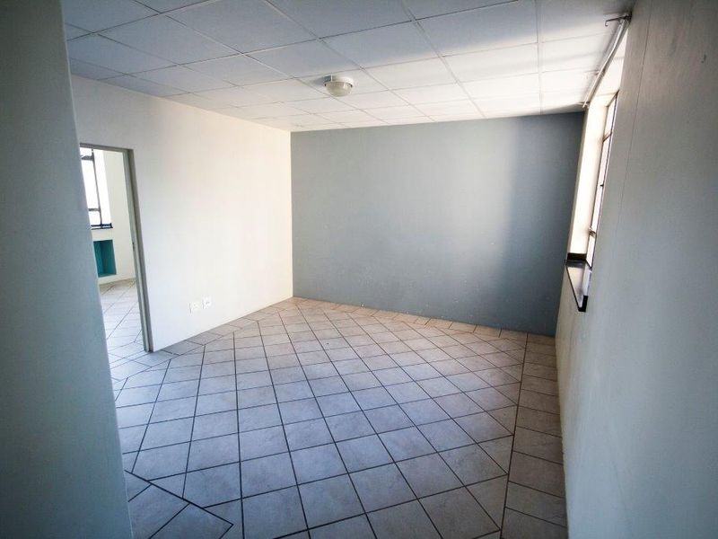 An empty room featuring tiled flooring, a drop ceiling, and a neutral color palette, offering a blank canvas for potential renovation or styling.