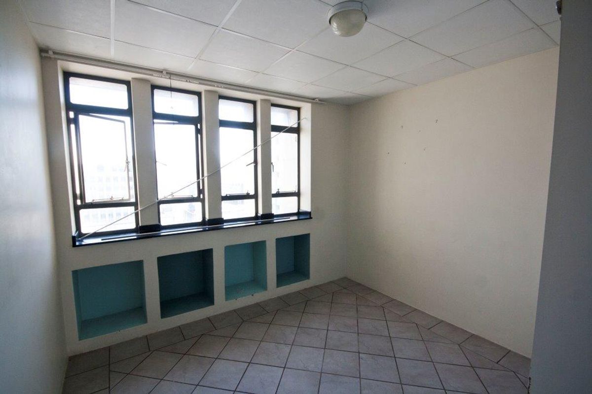An empty bedroom featuring tiled flooring, built-in wall niches, and large windows providing natural light.