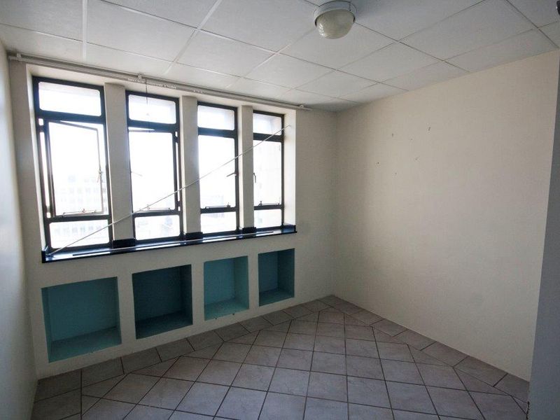 An empty bedroom featuring tiled flooring, built-in wall niches, and large windows providing natural light.