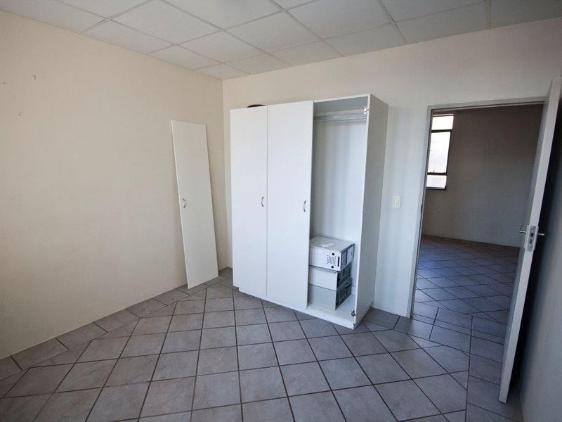 A basic bedroom featuring tiled flooring, a drop ceiling, and a built-in wardrobe with a detached door panel.
