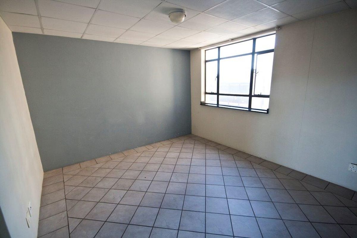 An empty bedroom featuring tiled flooring, a drop ceiling, and a large window providing natural light.