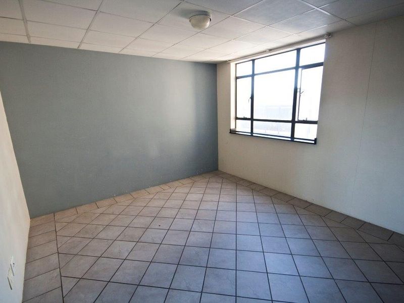 An empty bedroom featuring tiled flooring, a drop ceiling, and a large window providing natural light.