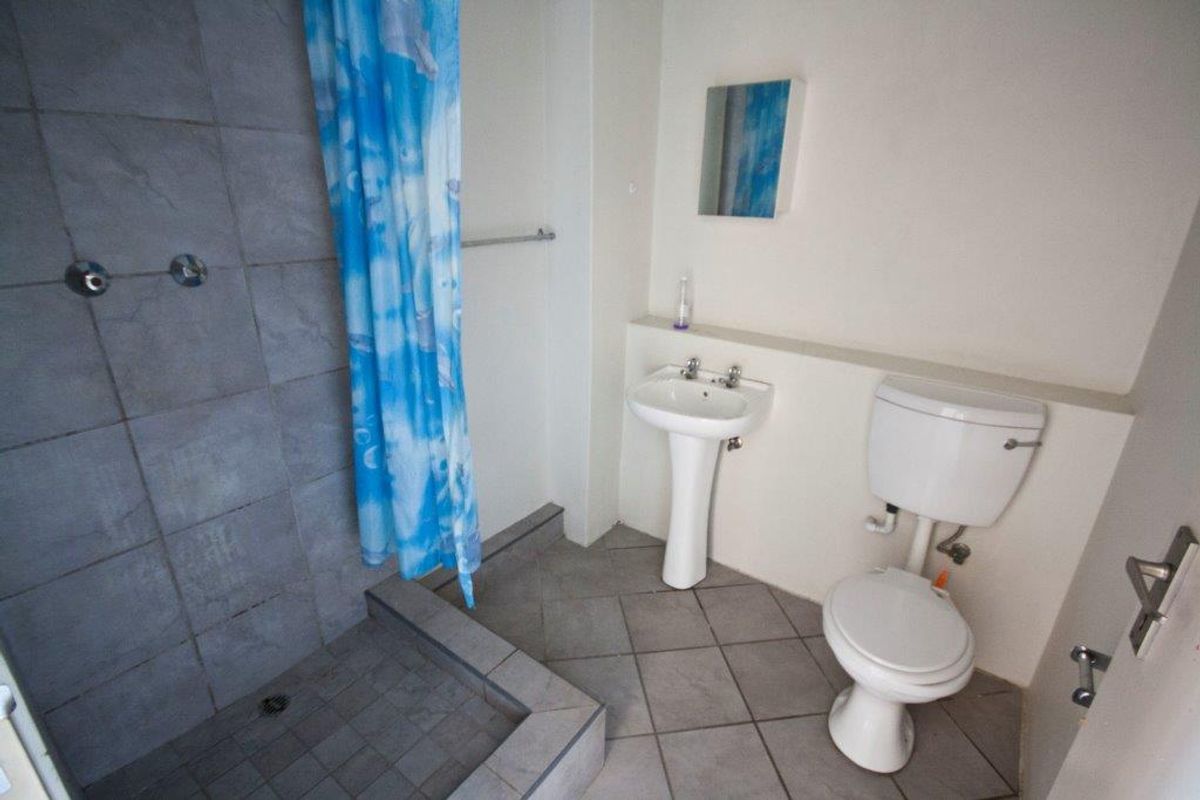 A functional bathroom featuring a walk-in shower with tiled surround, pedestal basin, and standard toilet.
