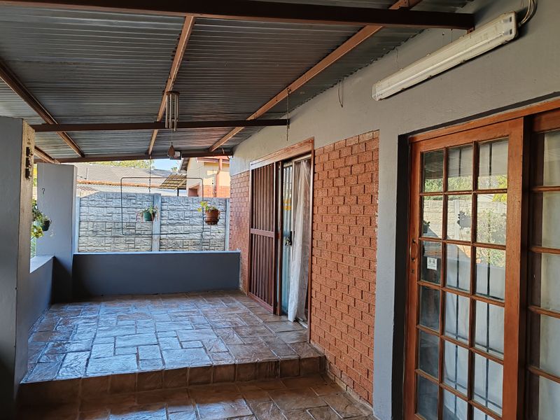 A covered patio area featuring tiled flooring, exposed brickwork, and access to the interior through sliding and timber-framed glass doors.