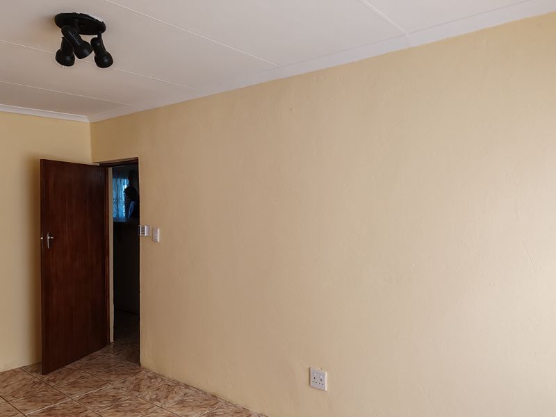 An empty living room featuring tiled flooring, a wooden door, and a ceiling light fixture, presenting a blank canvas for interior design.