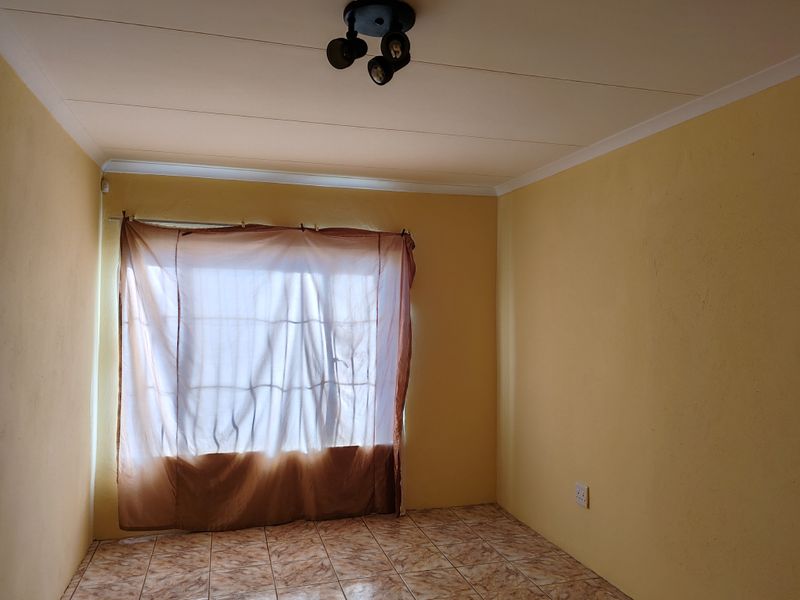 An empty bedroom featuring tiled flooring, a ceiling-mounted spotlight fixture, and yellow painted walls, offering a blank canvas for potential interior design updates.