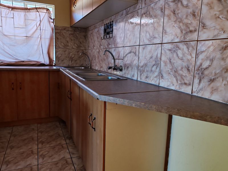 A functional kitchen featuring built-in cabinetry, laminate countertops, a double stainless steel sink, and tiled finishes throughout.